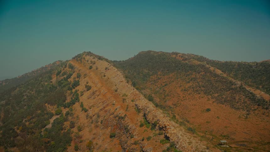 A static shot of a vast, golden-brown mountain range stretches out under a clear, hazy blue sky