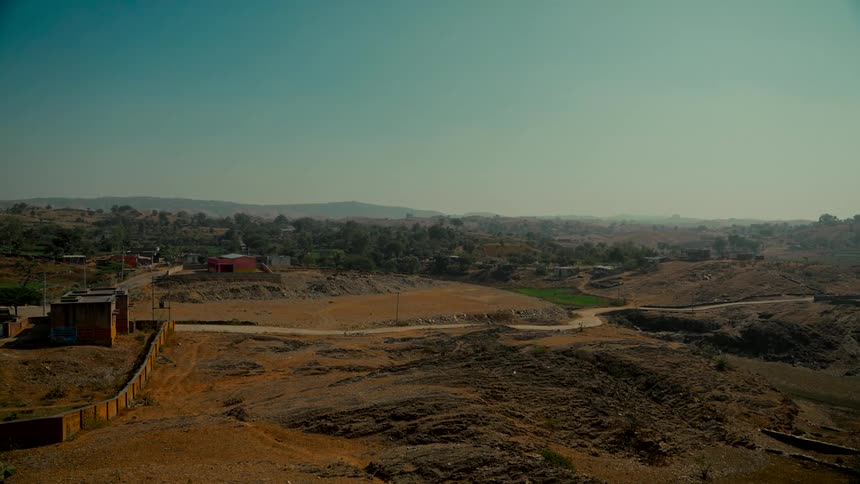 A wide shot of a small rural village in a vast, arid, and hilly landscape on a clear day