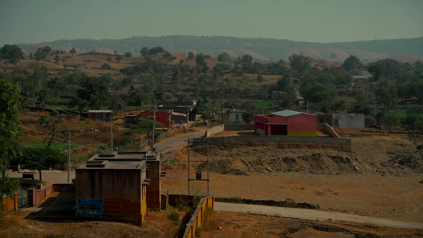 A lone motorbike drives up a winding road through a remote village nestled in the dry, rolling hills