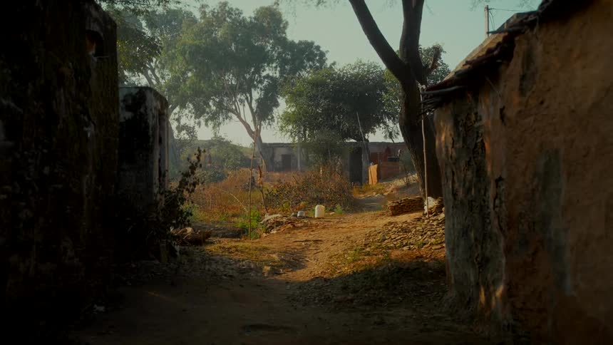 Sunlight illuminates a tranquil and dusty alleyway in a rustic village with traditional mud brick homes