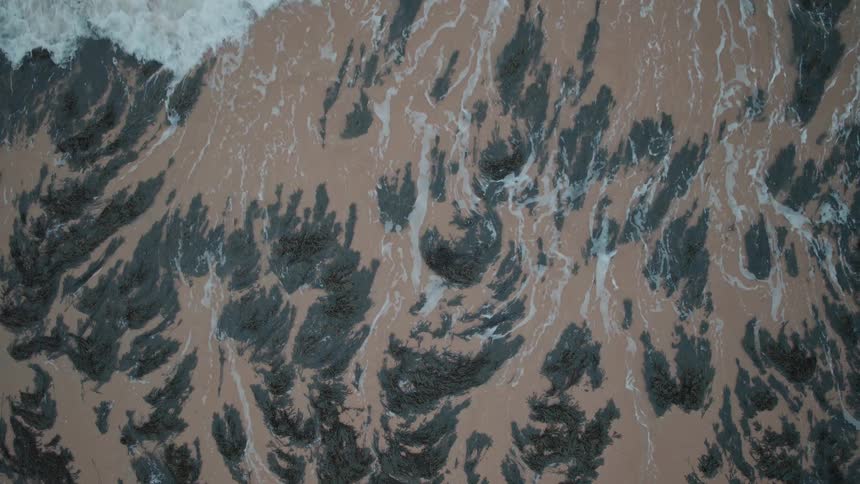 Mesmerizing top-down view of gentle ocean waves washing ashore in slow motion, creating an abstract pattern as the water recedes