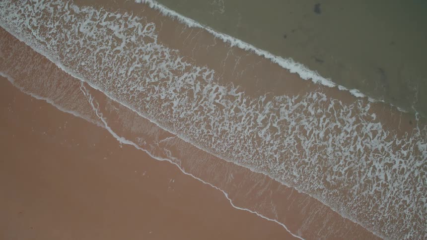 A calming top-down aerial view of gentle ocean waves slowly rolling onto a sandy beach