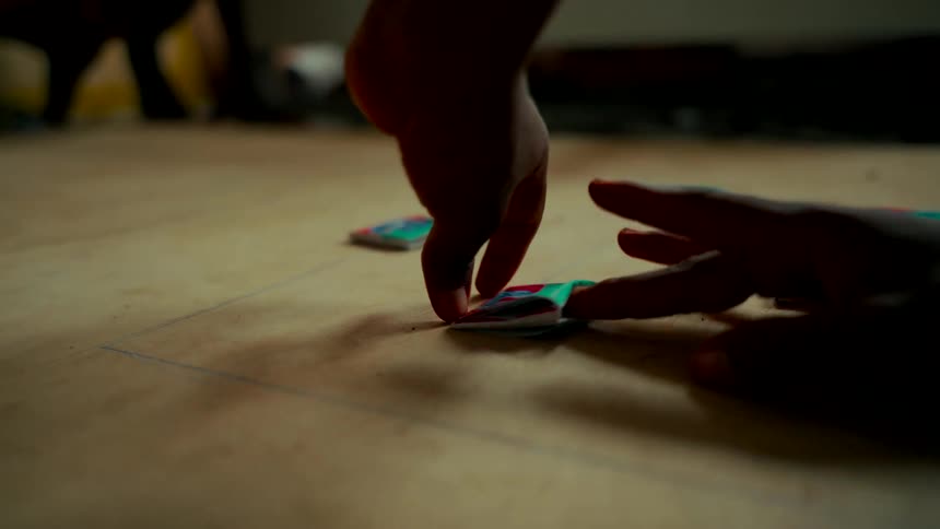 A close-up slow-motion shot of a person's hands flicking a colorful paper game piece across a wooden surface