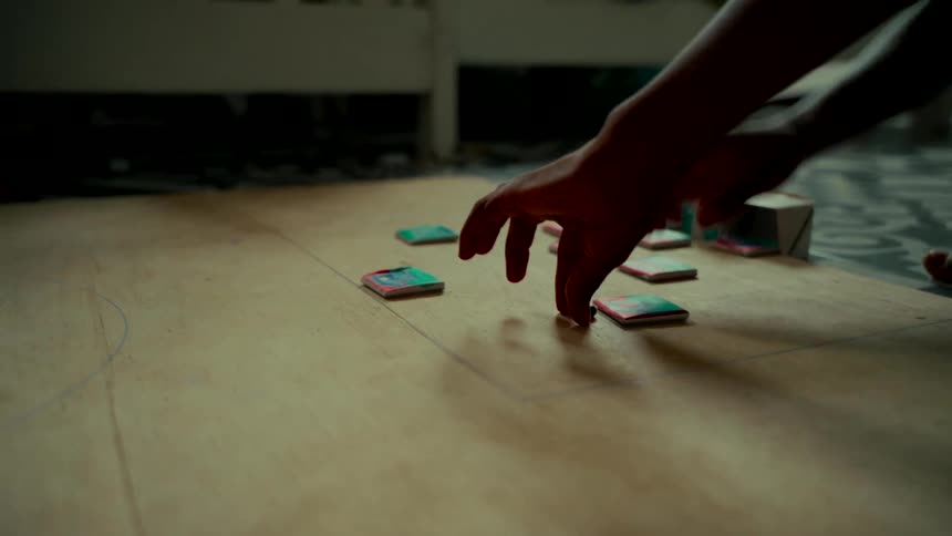 A close-up shot of a child's hands playing a handmade tabletop game on a wooden floor in slow motion