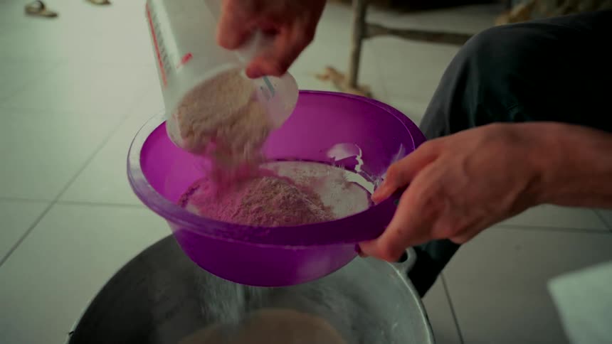 A baker carefully sifts flour from a measuring cup through a purple sieve in slow motion