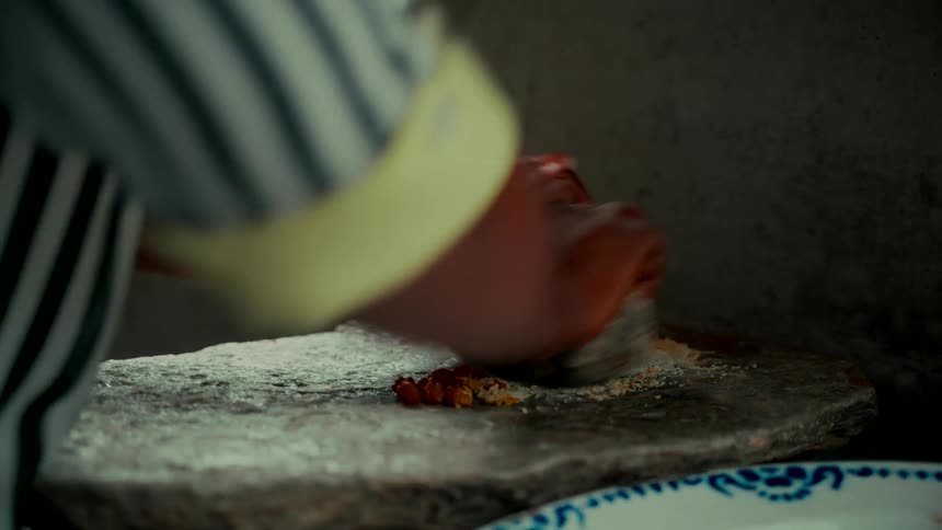 A woman uses a traditional stone grinder to crush peanuts for cooking in a rustic setting