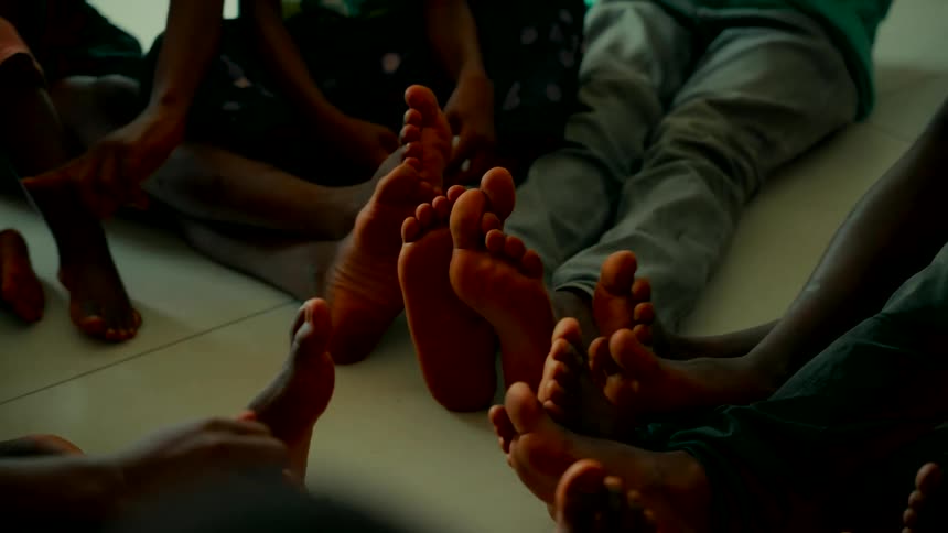 A close-up of the bare feet of a group of children sitting together in a circle on the floor