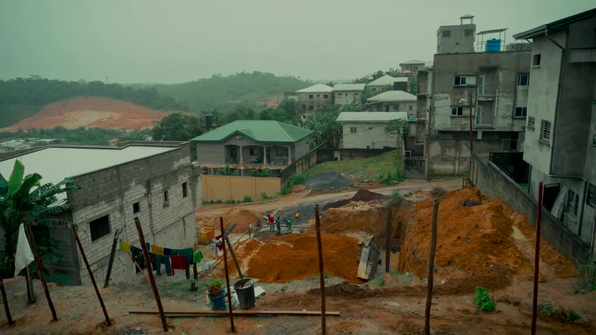 Workers on a construction site in a developing residential area nestled in lush, green hills on an overcast day
