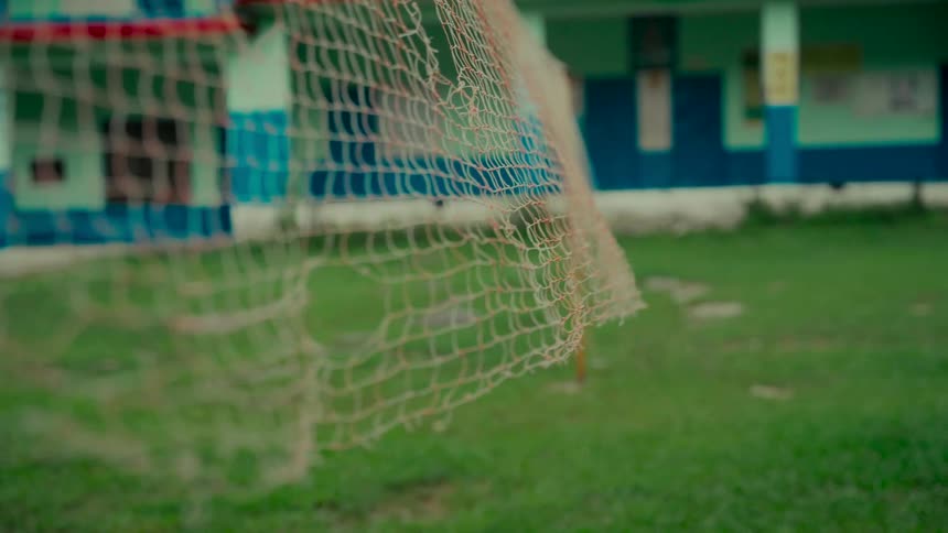A close-up of a worn and torn volleyball net on an empty grassy schoolyard