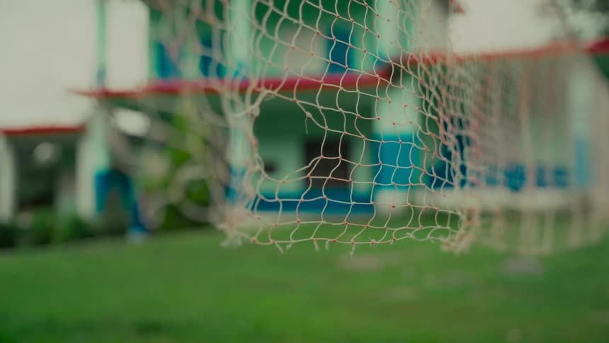 A close-up shot of a tattered and torn badminton net on a green lawn with a building in the background