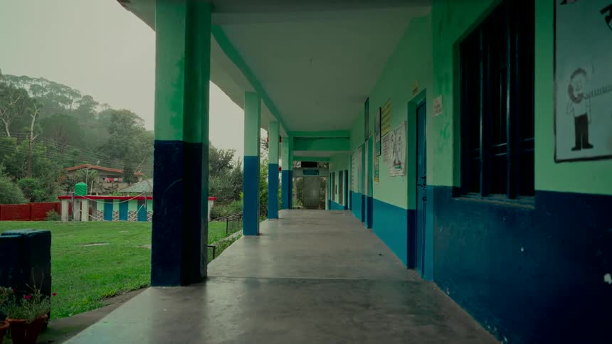 A static shot of a deserted, colorful school corridor overlooking a grassy yard on an overcast day