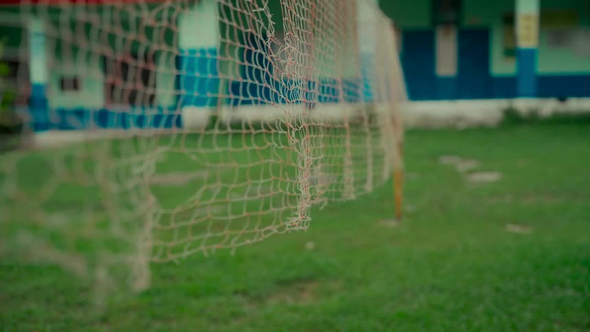 A close-up shot focuses on a broken badminton net on a green grassy field at a school playground