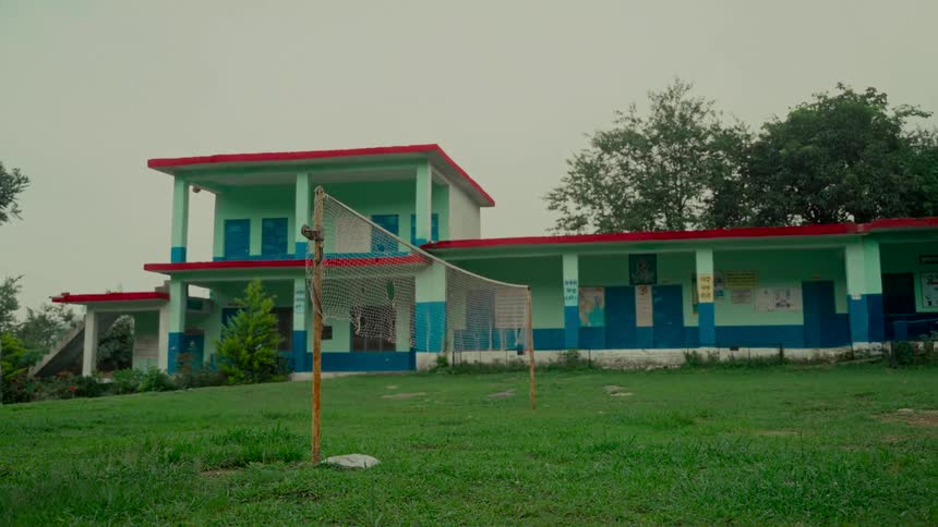 An empty schoolyard with a volleyball net stands before a colorful school building in rural India