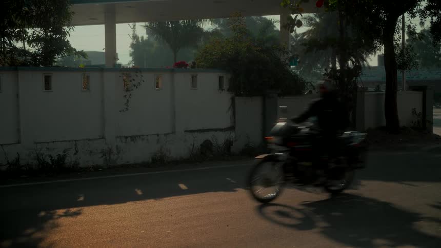 A motorcycle rides down a quiet road in slow motion during a hazy golden hour