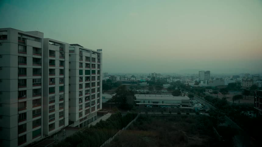 A wide shot of a hazy cityscape at dawn with a large apartment building in the foreground
