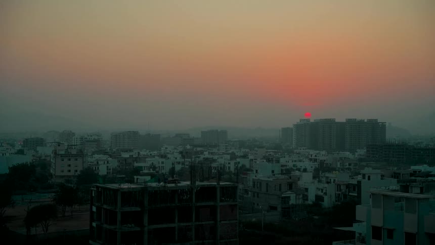 A red sun rises over a hazy city skyline at dawn