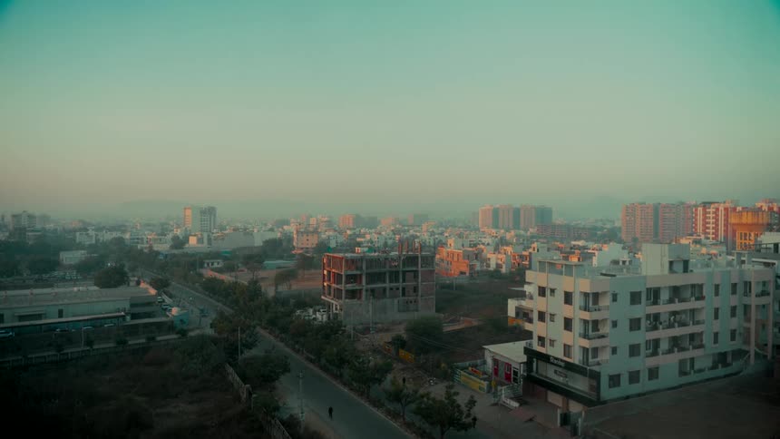 A tranquil, wide-angle view of a developing city skyline bathed in the warm, hazy light of sunrise