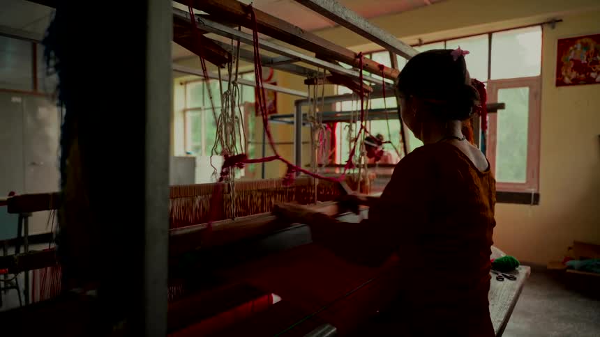 Silhouette of a woman weaving vibrant red fabric on a traditional wooden handloom in a sunlit workshop