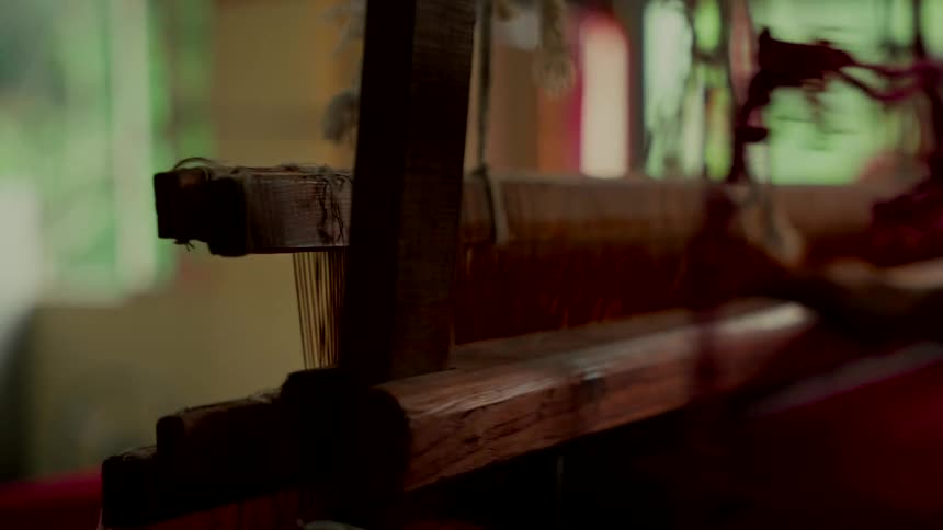 A close-up of a traditional wooden weaving loom in operation, its parts moving rhythmically to create fabric