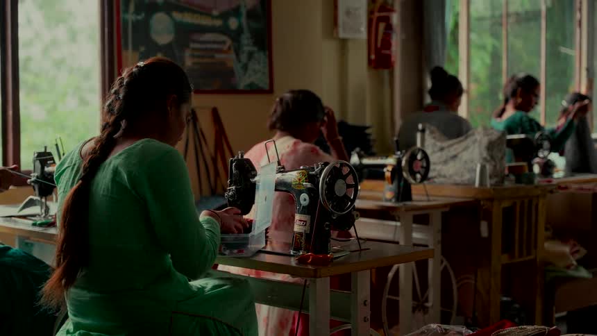 Women artisans work together in a busy textile workshop, each at their own sewing machine