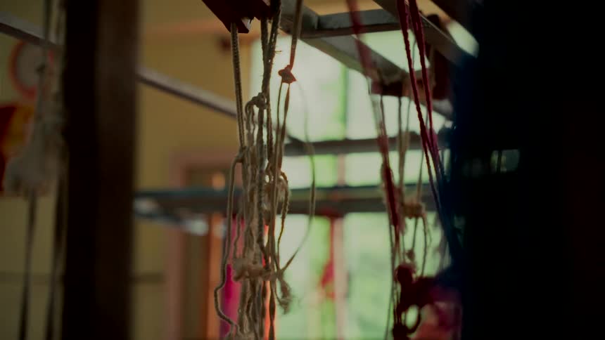 Close-up of intricate threads and ropes moving back and forth on a traditional handloom in a workshop