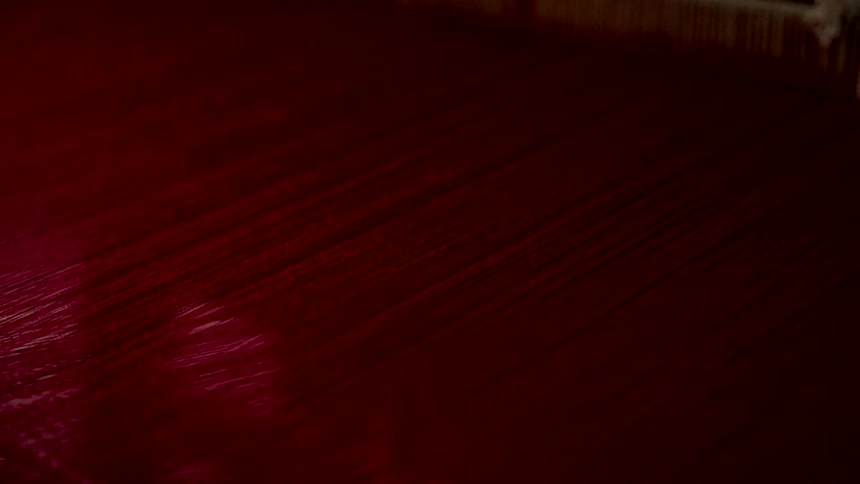 Extreme close-up of rich, deep red threads moving rhythmically on a traditional weaving loom