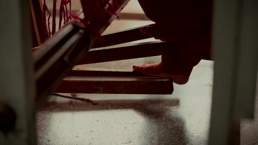 A close-up of a weaver's bare feet operating the wooden pedals of a traditional loom