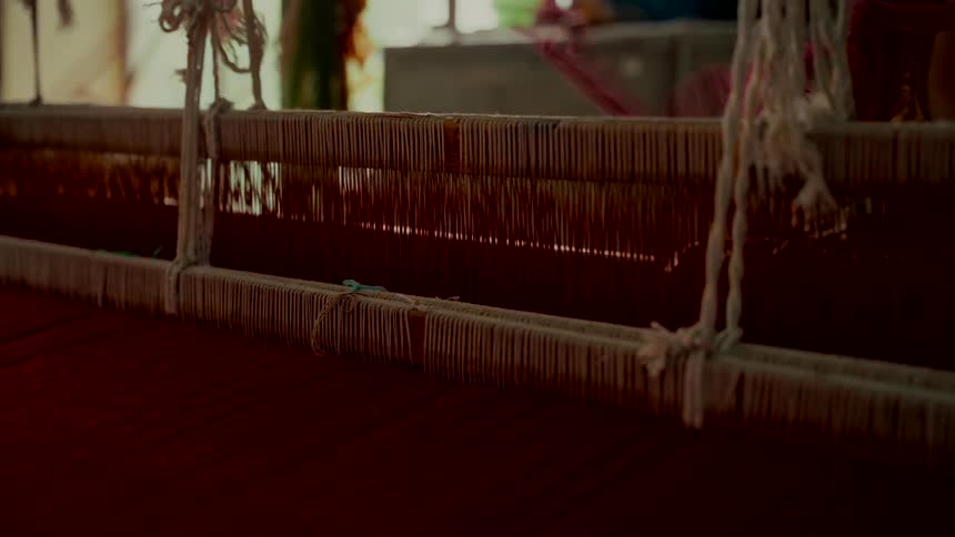 Close-up on the intricate, rhythmic motion of a traditional handloom weaving vibrant red fabric in a workshop