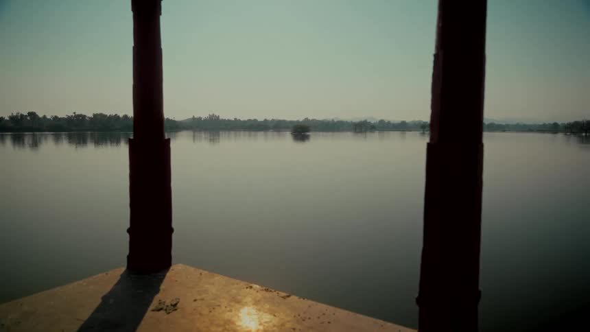 A tranquil and still lake is viewed between two red pillars on a clear day