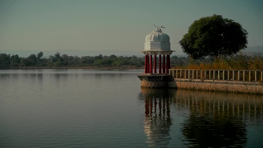 A tranquil shot of a beautiful ornate gazebo reflecting on a calm lake during a golden hour sunset