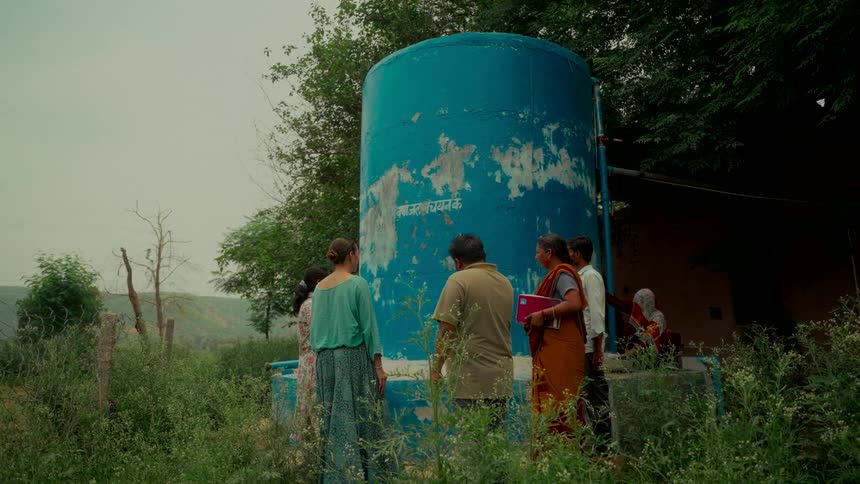A group of villagers and an aid worker inspect a large blue water tank in a rural community in India