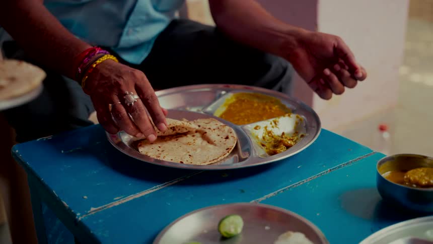 A person receives fresh roti on a traditional thali plate with dal and curry in slow motion
