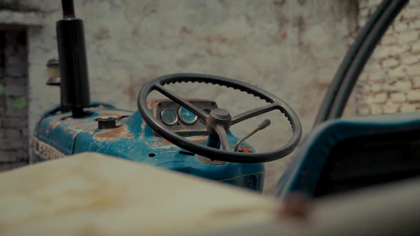 A close-up view of the steering wheel on a rusty, vintage blue tractor parked indoors