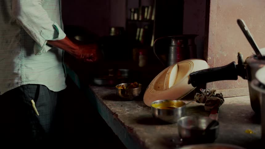 Close up slow motion shot of a man preparing food in a dimly lit, rustic Indian kitchen