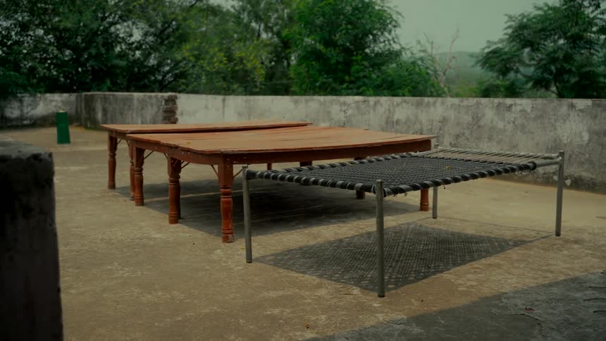 Traditional Indian wooden and woven cots sit empty on a concrete rooftop patio in a rural setting