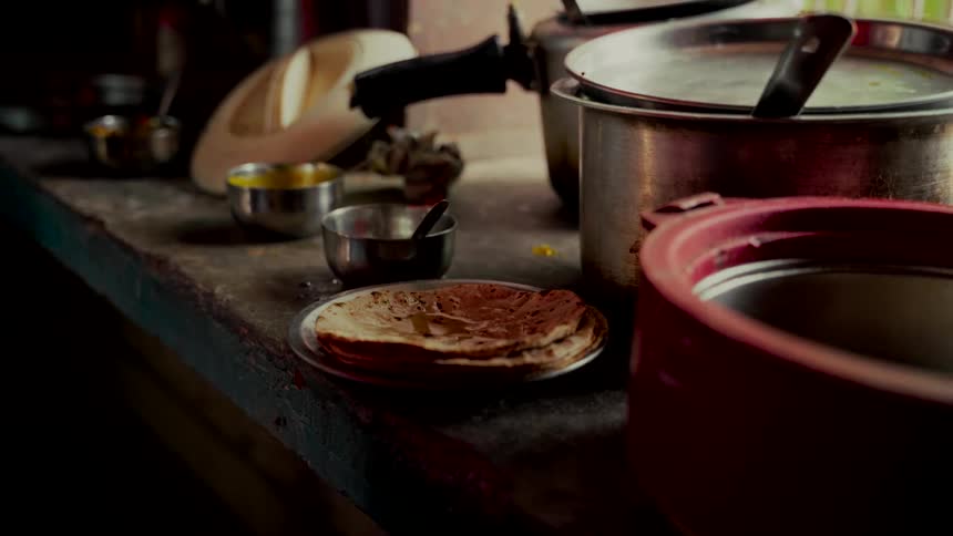 Freshly made Indian chapati being topped with ghee in a rustic, dimly lit kitchen