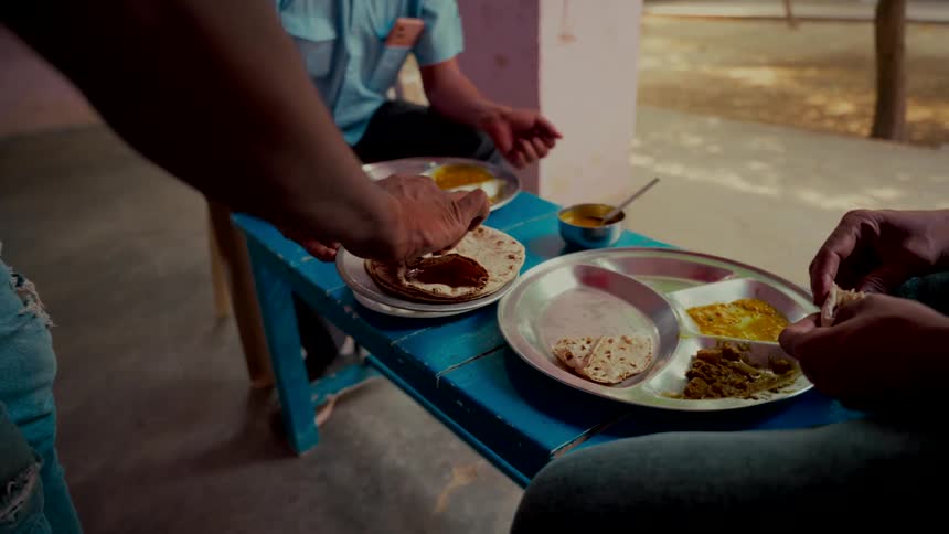 Slow-motion close-up of men sharing a traditional Indian meal of roti, dal, and vegetables served on thali plates