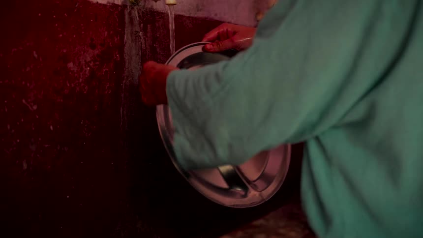 Slow motion shot of two people washing their metal trays under running water from old faucets