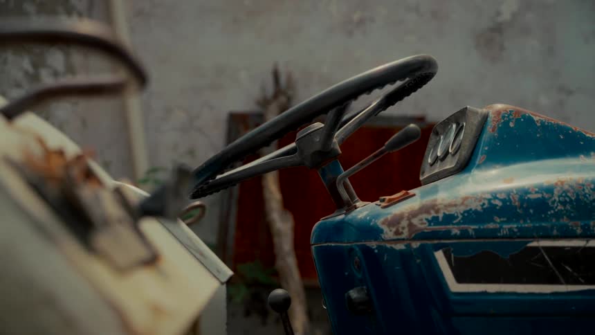 A close-up view of a steering wheel on a rusty, old blue tractor abandoned in a scrapyard