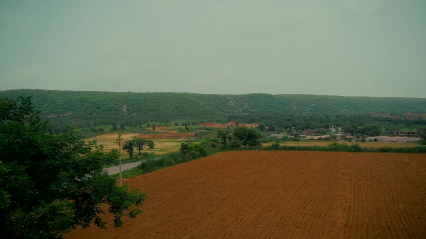 A serene, wide shot of a plowed agricultural field in front of a lush green hillside in the rural countryside