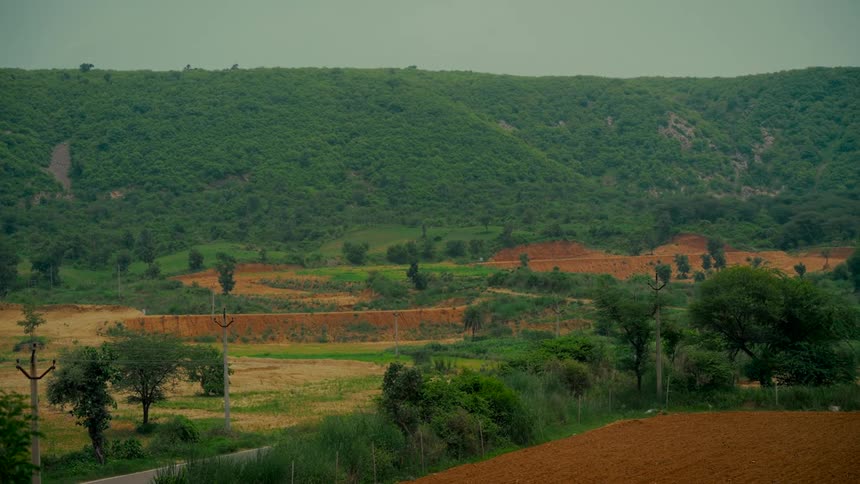 A wide shot of vehicles driving on a rural road through a lush green valley with rolling hills