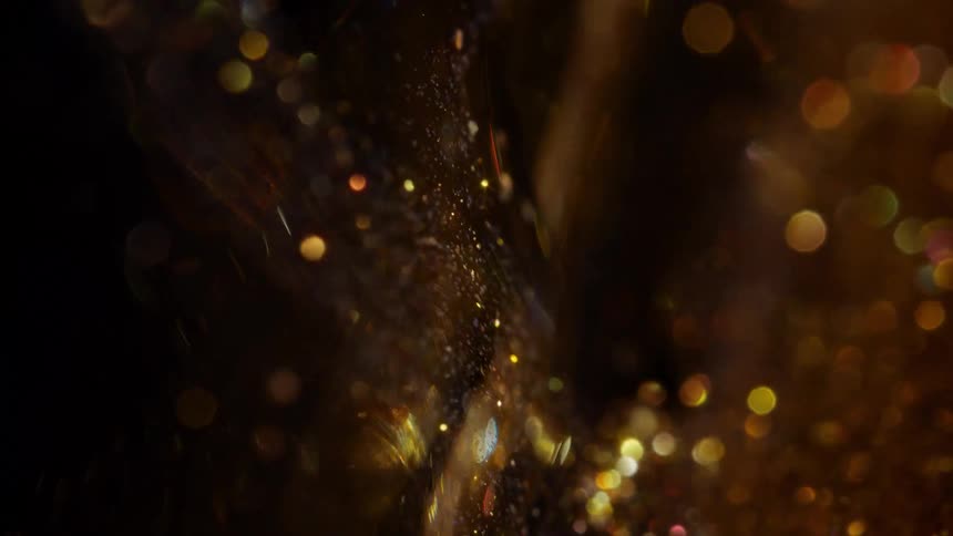 Abstract background of sparkling gold bokeh lights and glittering particles drifting in slow motion