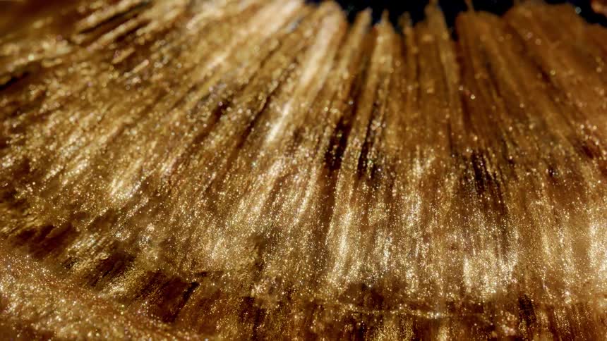Shimmering golden glitter fluid flows in a beautiful abstract closeup