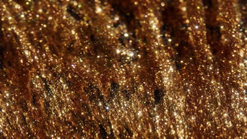 Sparkling gold glitter particles shimmer and create a luxurious, festive abstract background