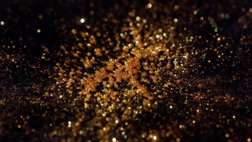 A beautiful golden glitter snowflake sparkles and shimmers with a bokeh effect against a dark background
