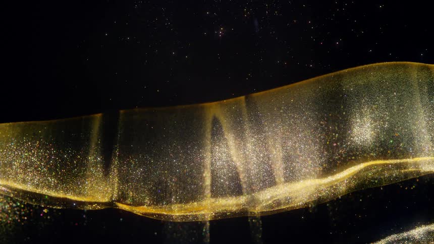 An elegant and abstract wave of sparkling golden glitter flows and rains down against a black background