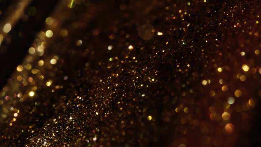 A macro close-up of golden glitter particles shimmering and sparkling with a beautiful bokeh effect