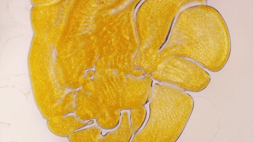 A mesmerizing macro shot of shimmering golden liquid flowing and expanding into organic, cell-like patterns on a white background