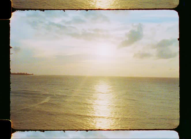 A peaceful sunrise reflects golden light across the calm ocean waves in a vintage film shot