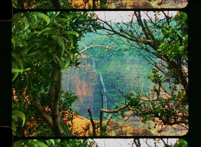 An 8mm vintage-style zoom-out shot of a beautiful waterfall cascading down a lush green canyon, framed by trees